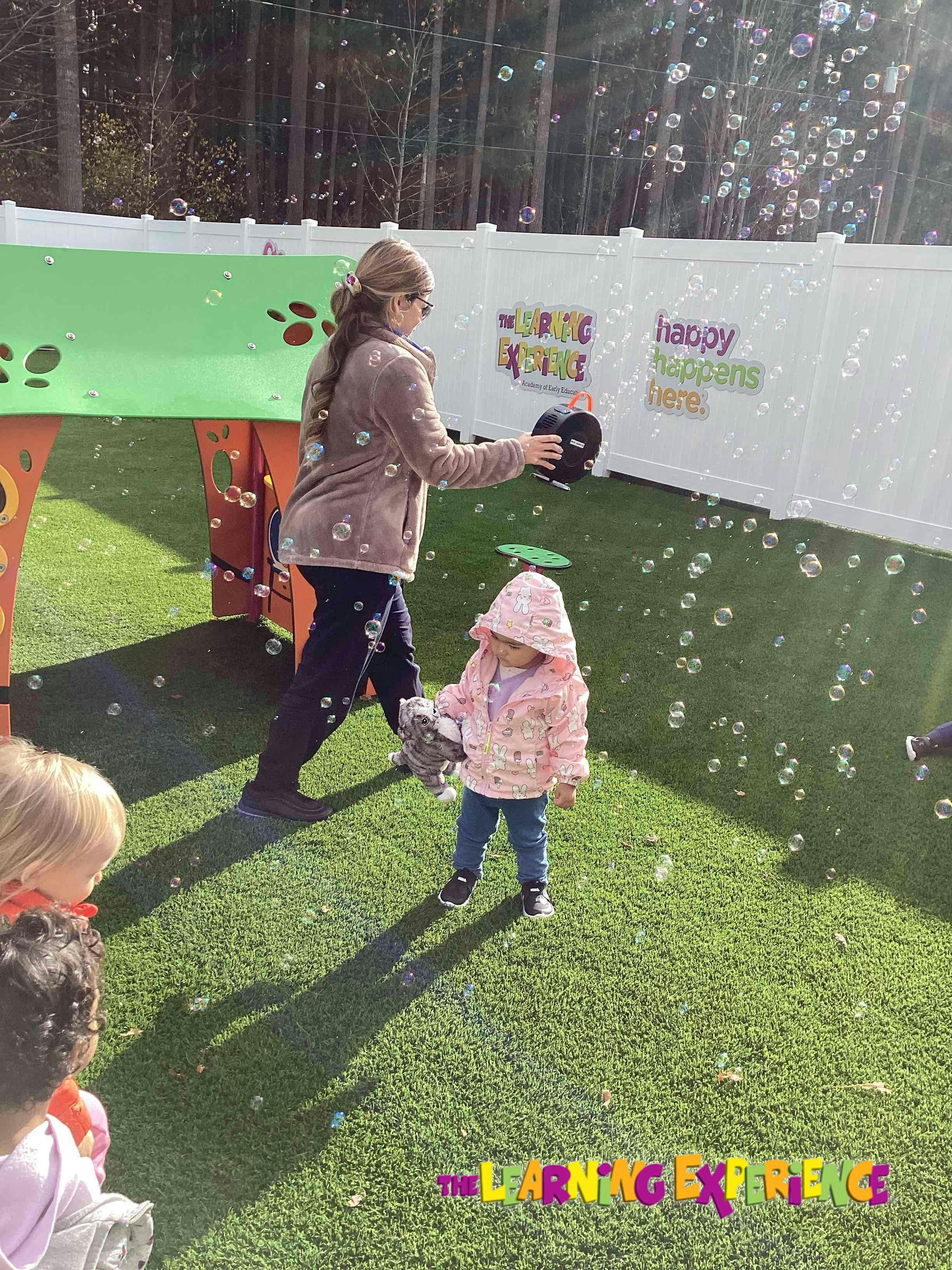 Person holding a bubble machine near a child on artificial turf