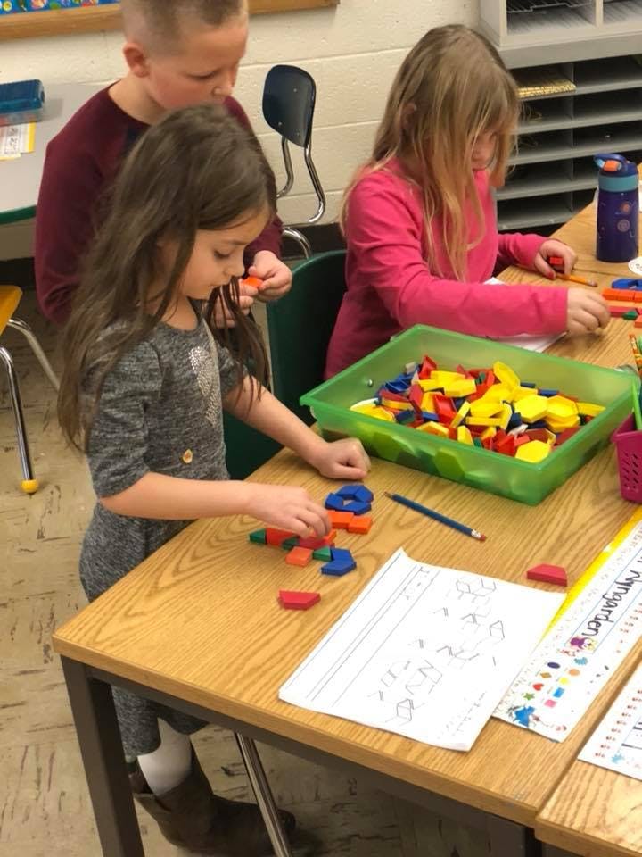 Three children at a table playing with colorful geometric shapes