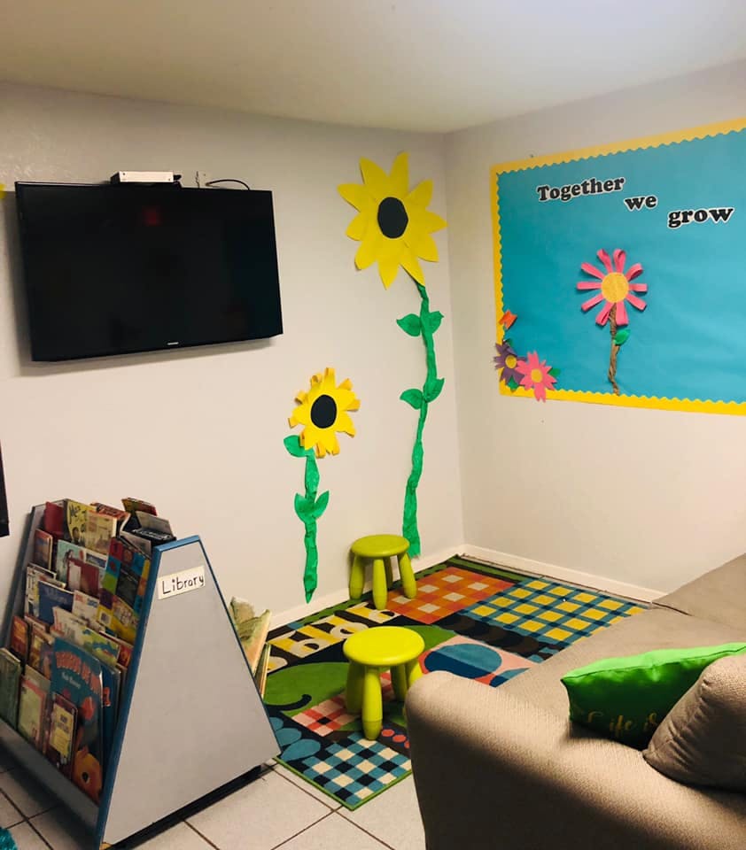 Children's room with a TV, book display, colorful rug, and sunflower wall decor