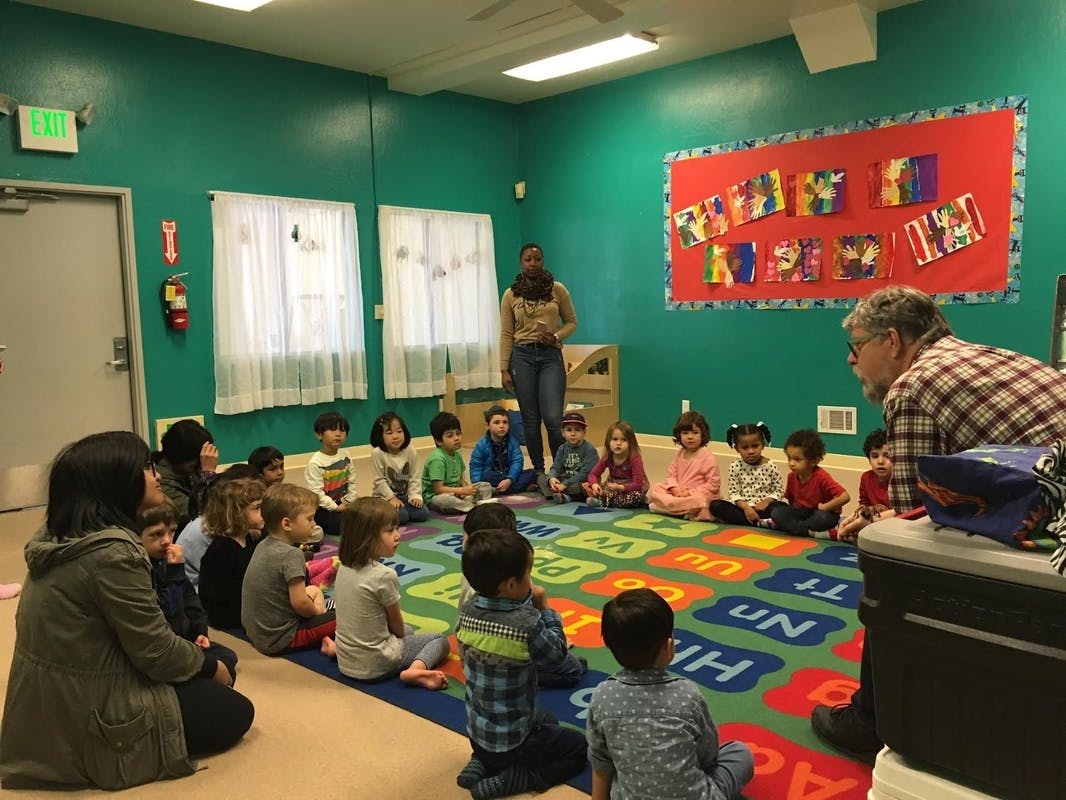 Adults and children sitting on a rug in a classroom