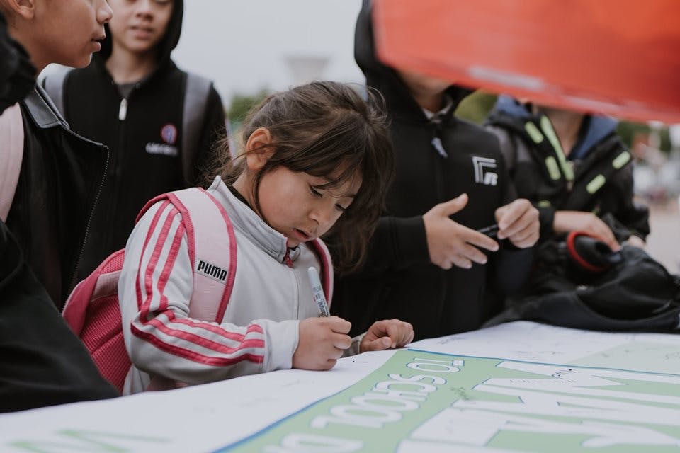 Child writing on a large paper with other people around