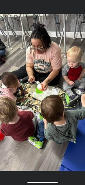 Person and three children sitting on the floor playing with sensory bin