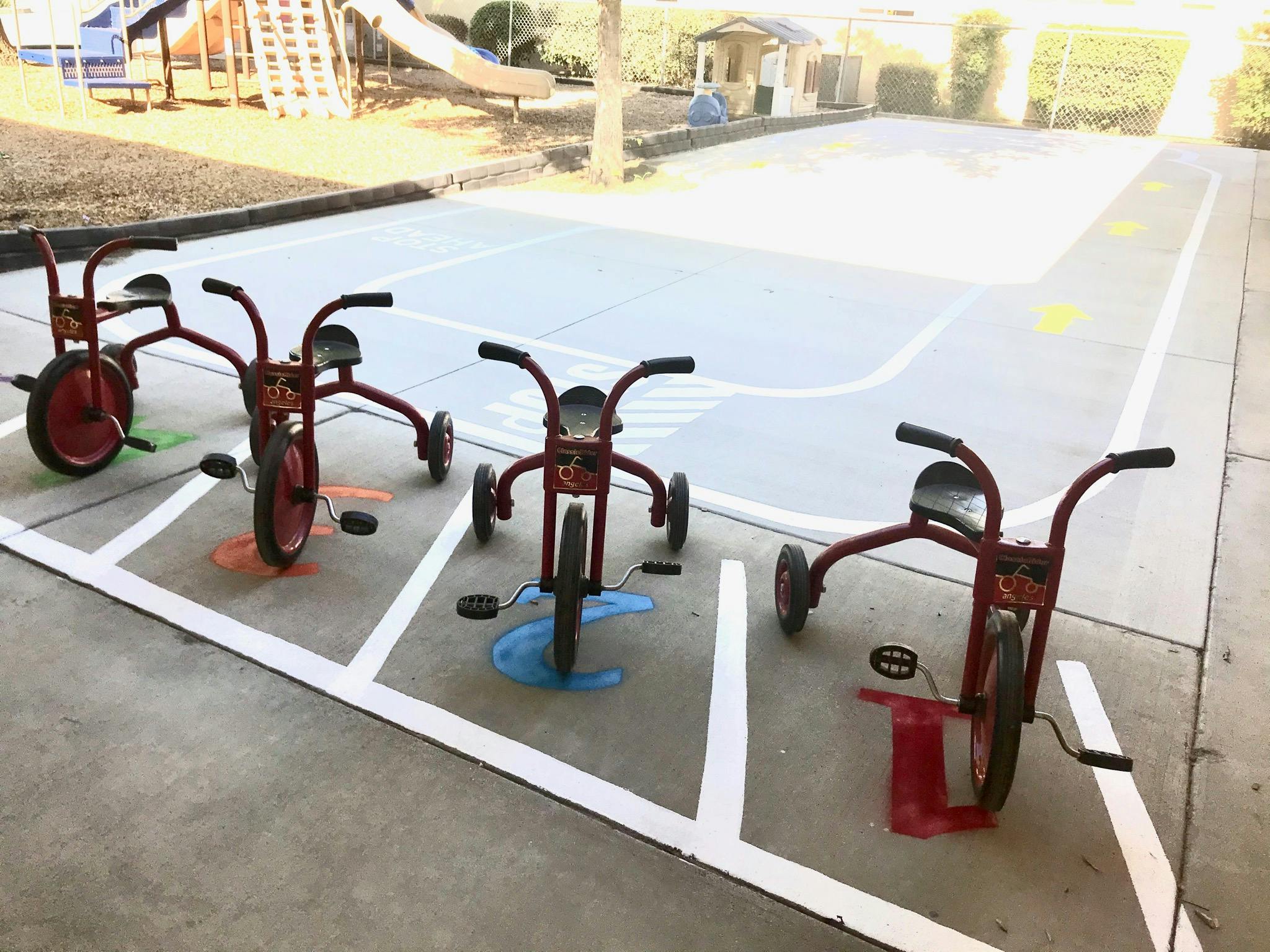 Four red tricycles parked in marked spaces on a playground
