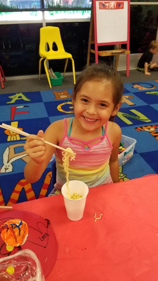 Child holding chopsticks with noodles over a cup