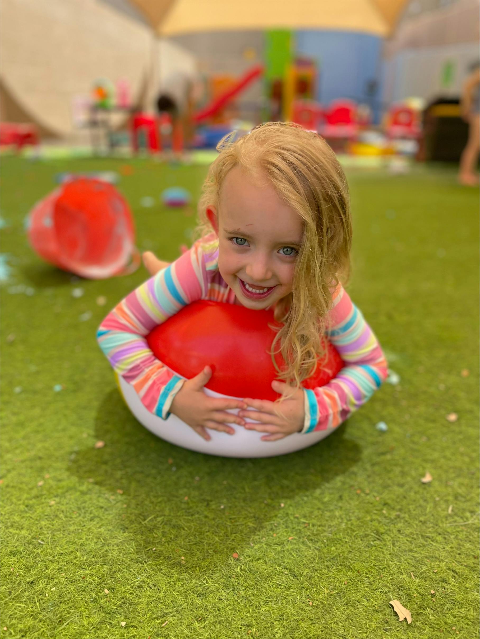 Child lying on stomach on a red and white ball on green grass