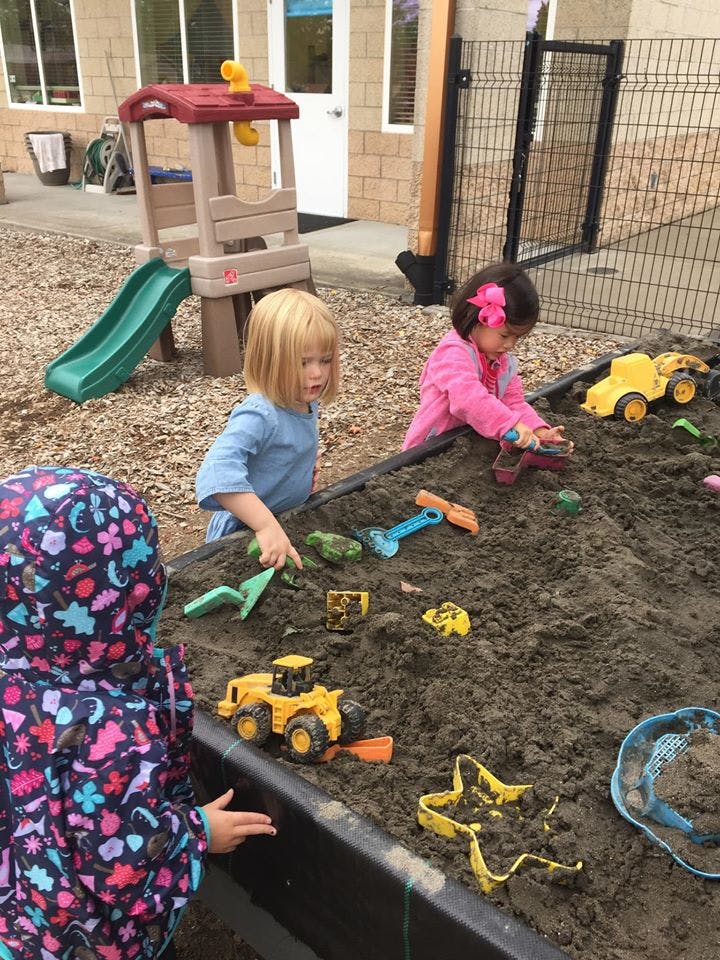 Three children playing in a sandbox with toys