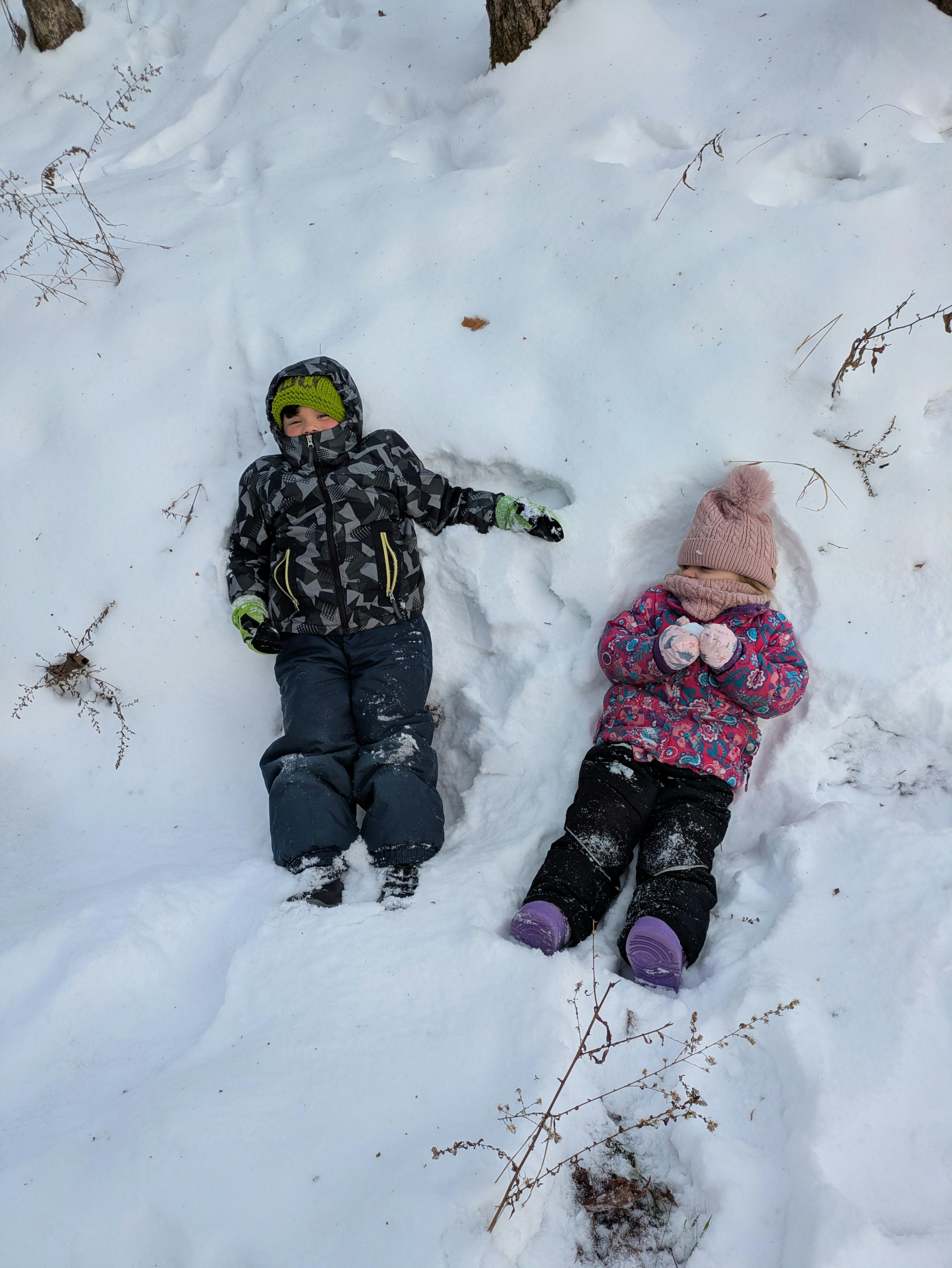 Two children dressed in winter clothes lying in the snow