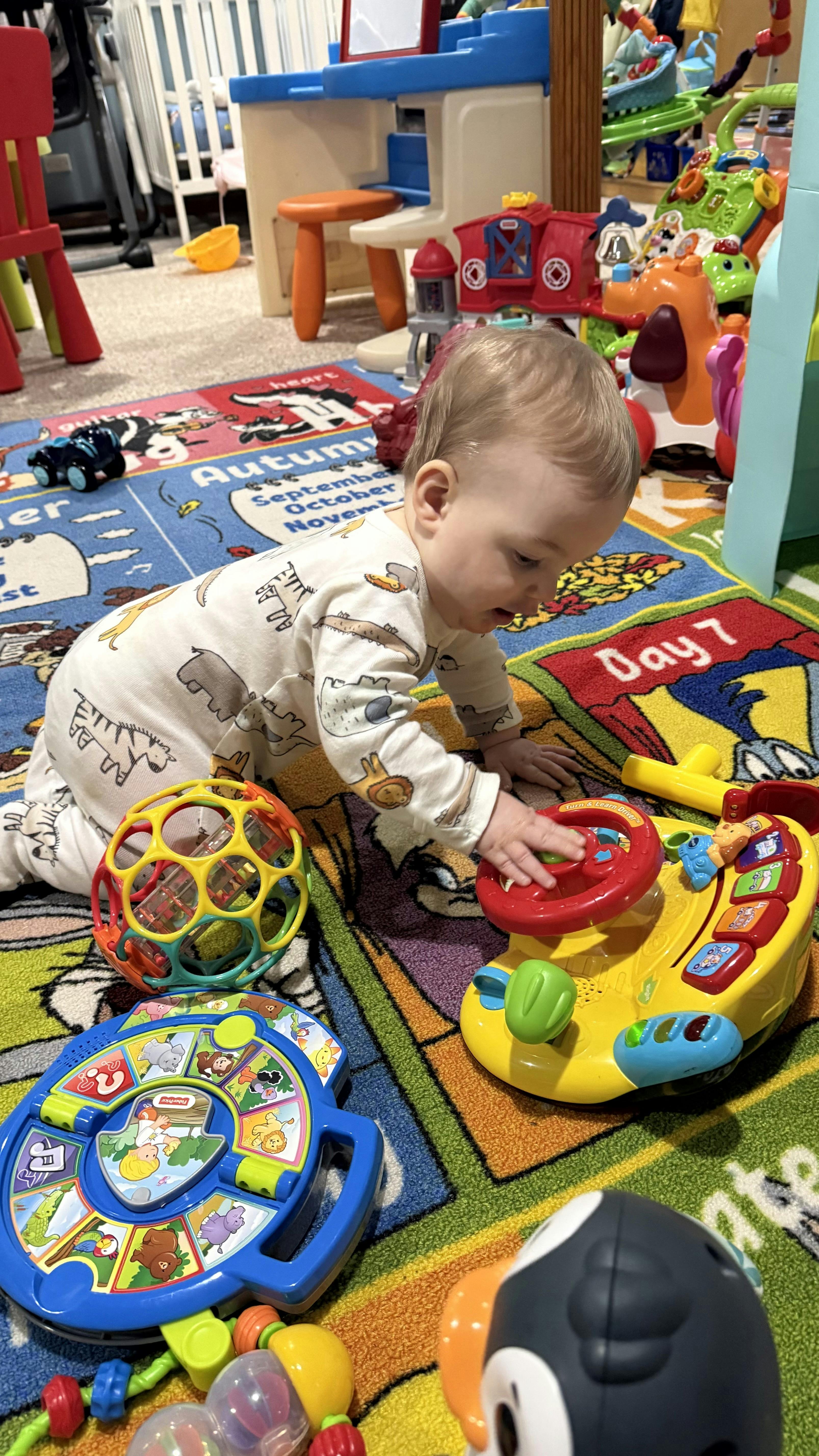Child crawling on a colorful ABC rug playing with a toy steering wheel