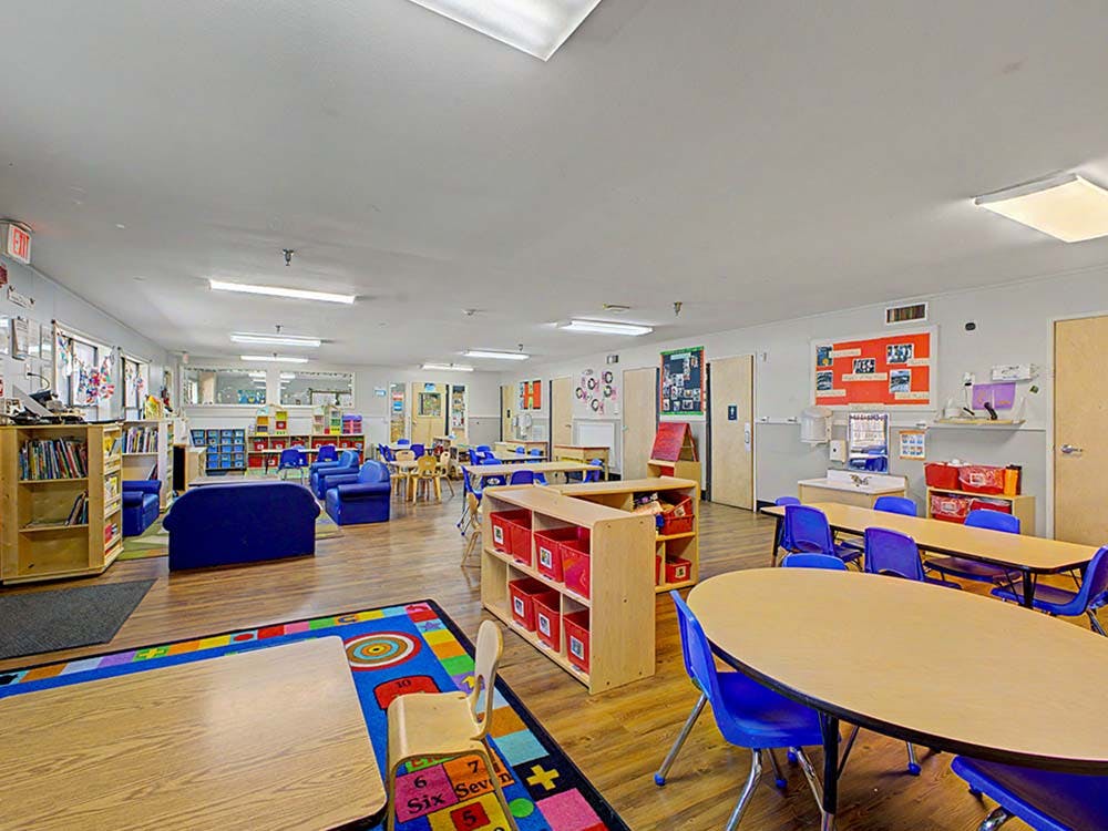 Classroom with small tables, chairs, bookshelves, and colorful rug
