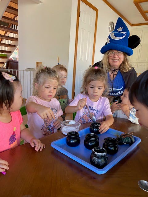 Adult in wizard hat with children at a table with small jars