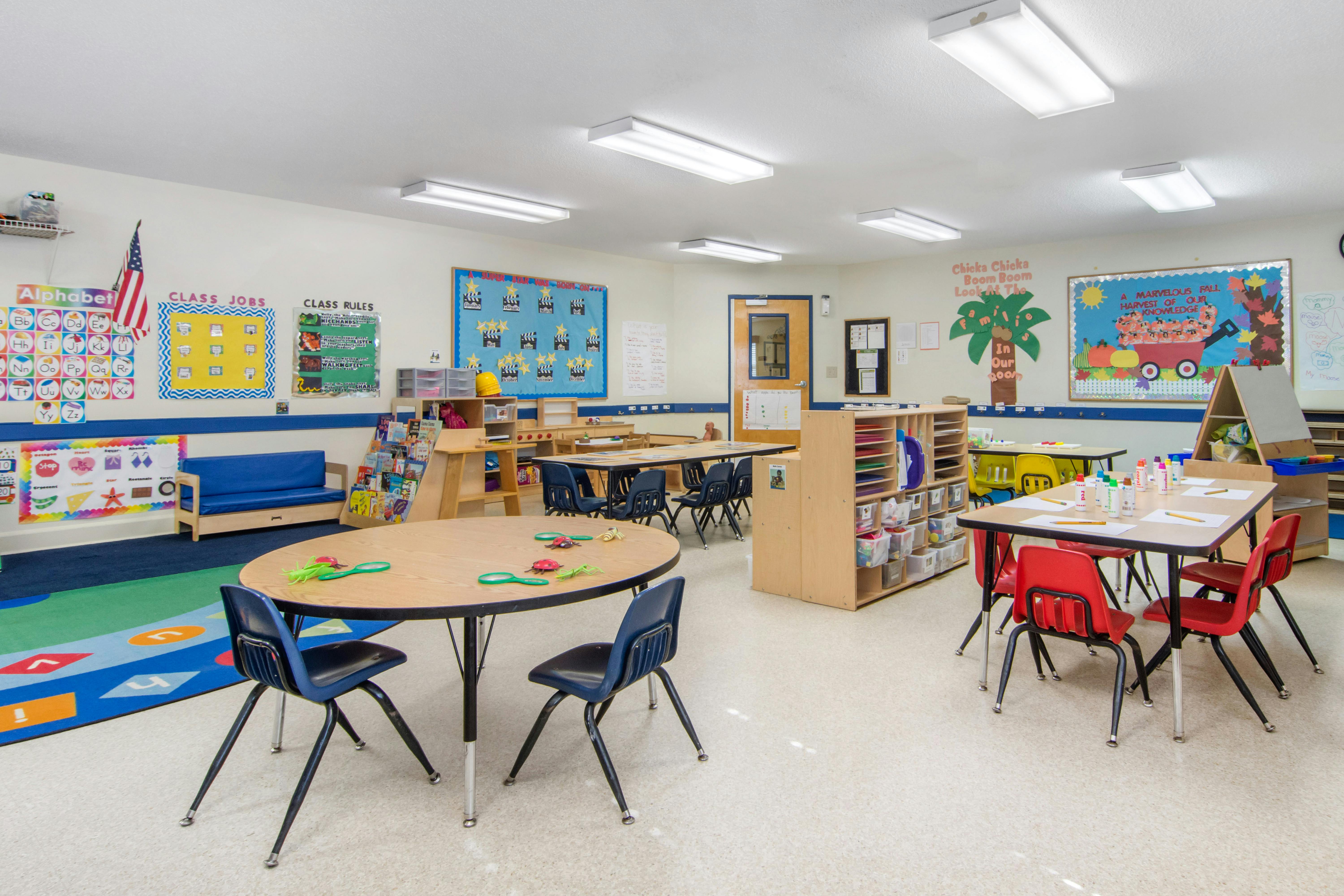 A colorful and well-organized preschool classroom with tables, chairs, and learning posters