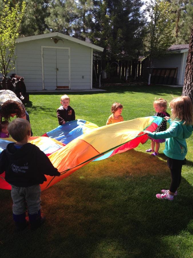 Children playing with a colorful parachute on a grassy lawn