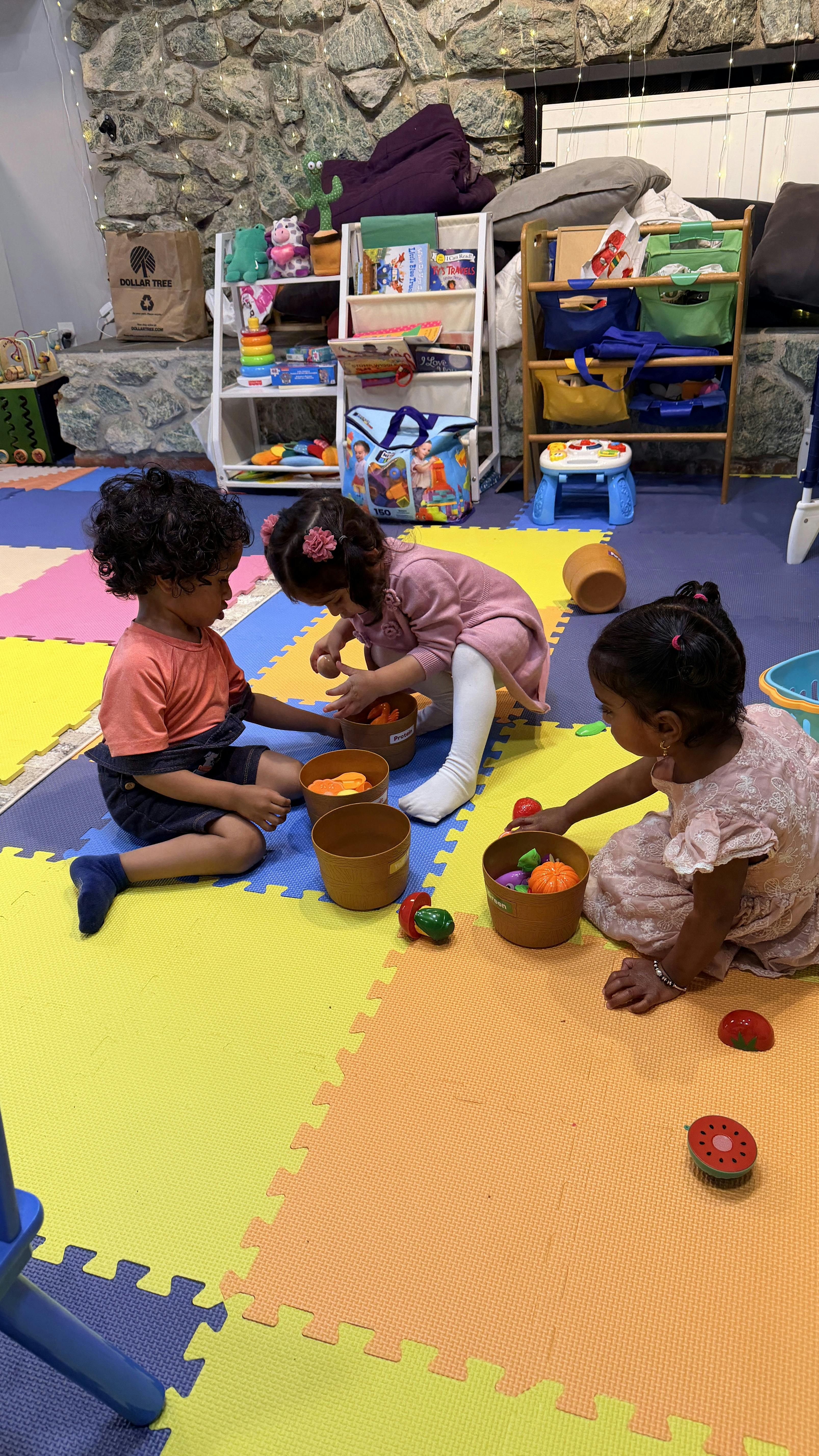 Three children playing with toy food in buckets on a colorful mat