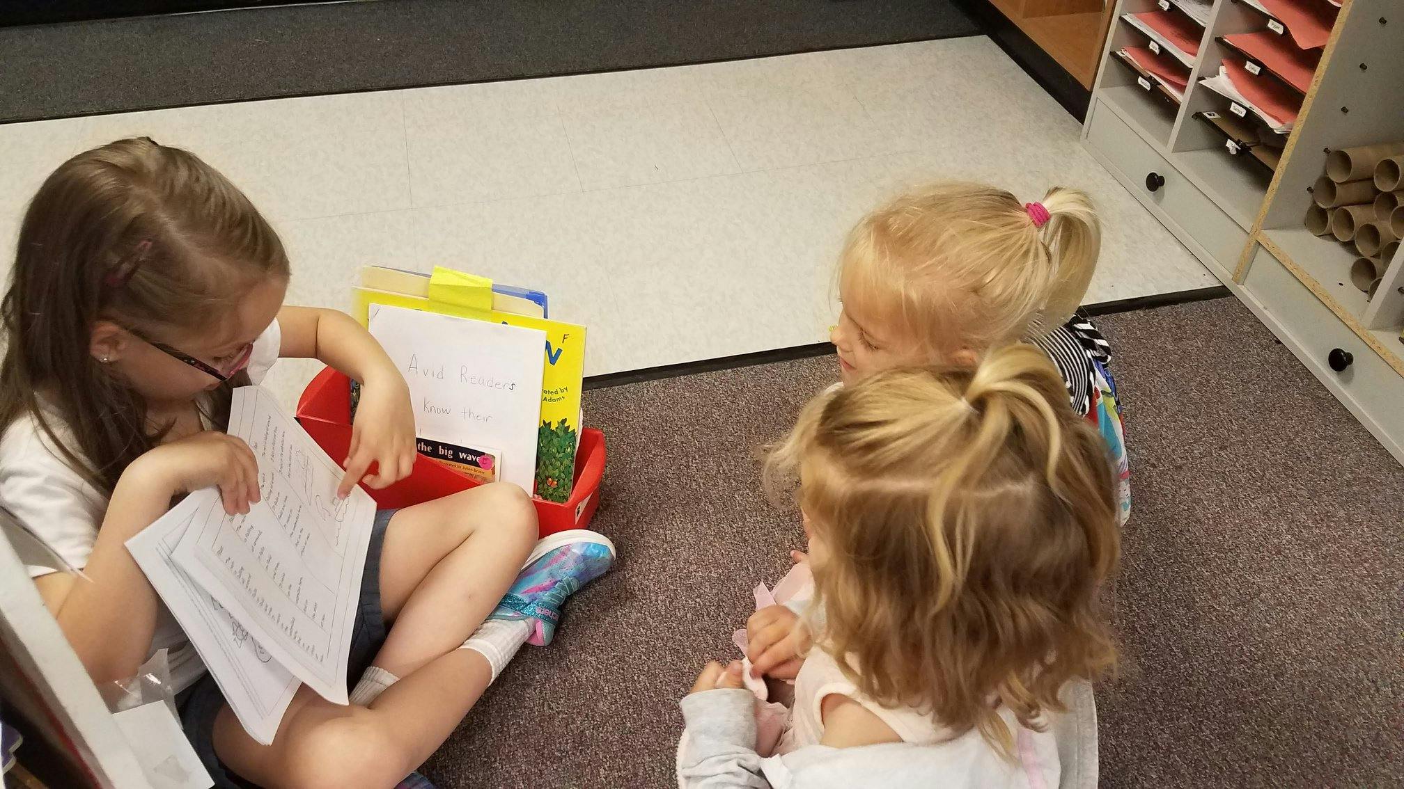Three children sitting on the floor looking at papers
