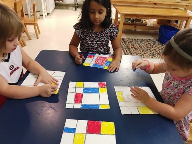 Three children coloring geometric patterns at a table