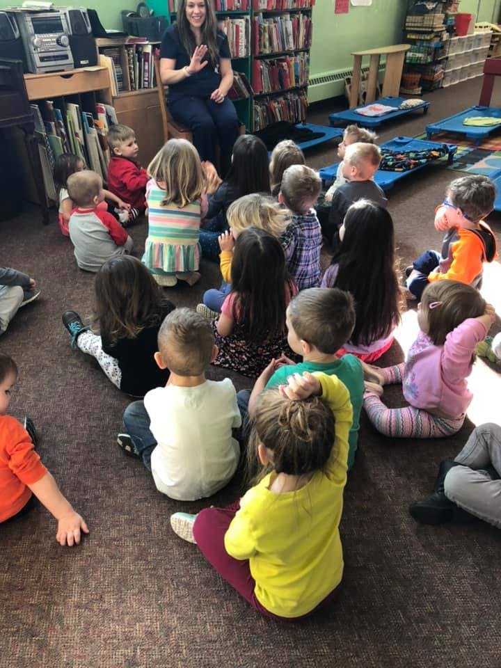 Adult speaking to a group of children sitting on the floor in a classroom
