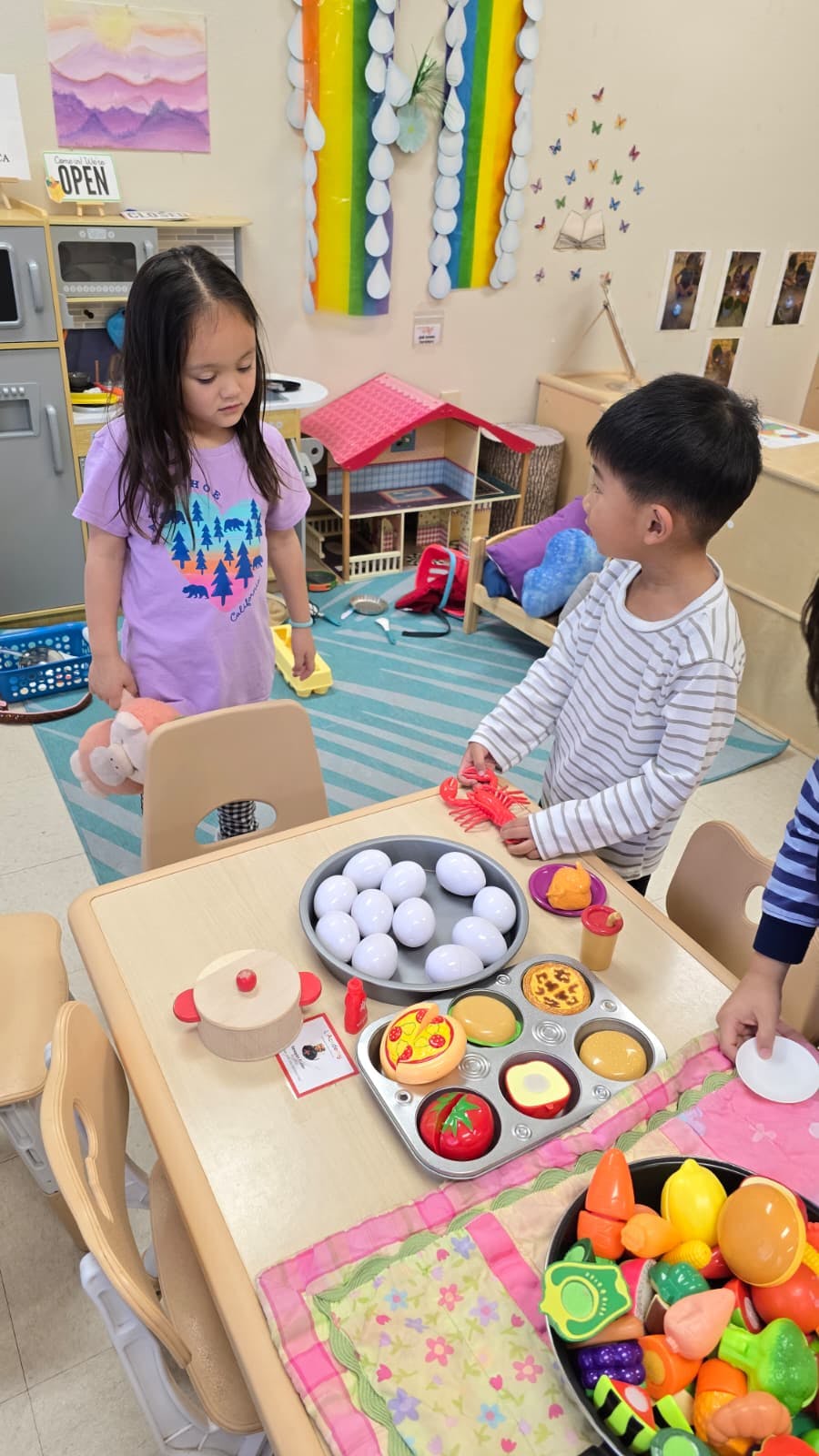 Two children playing with toy food at a table in a classroom