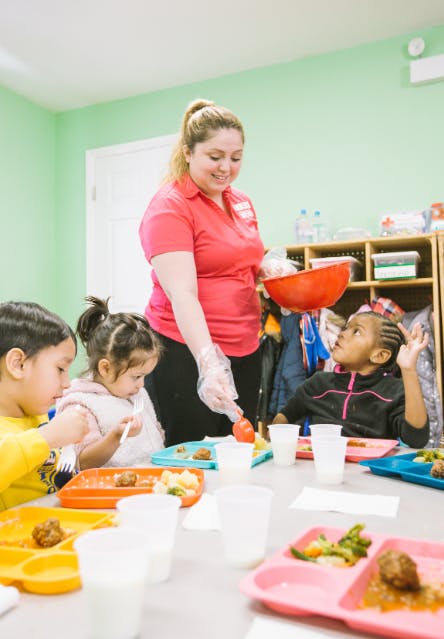 Adult serving food to children at a table