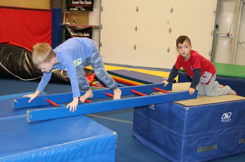Two children on blue gym equipment, one crawling on a ladder, one kneeling