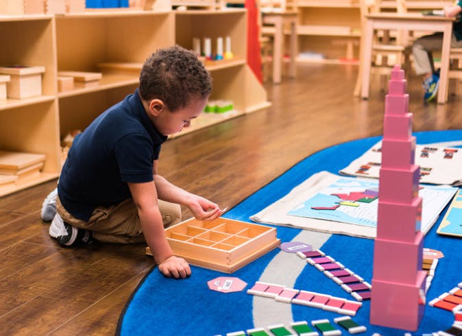 Child kneeling on floor, playing with wooden educational toys