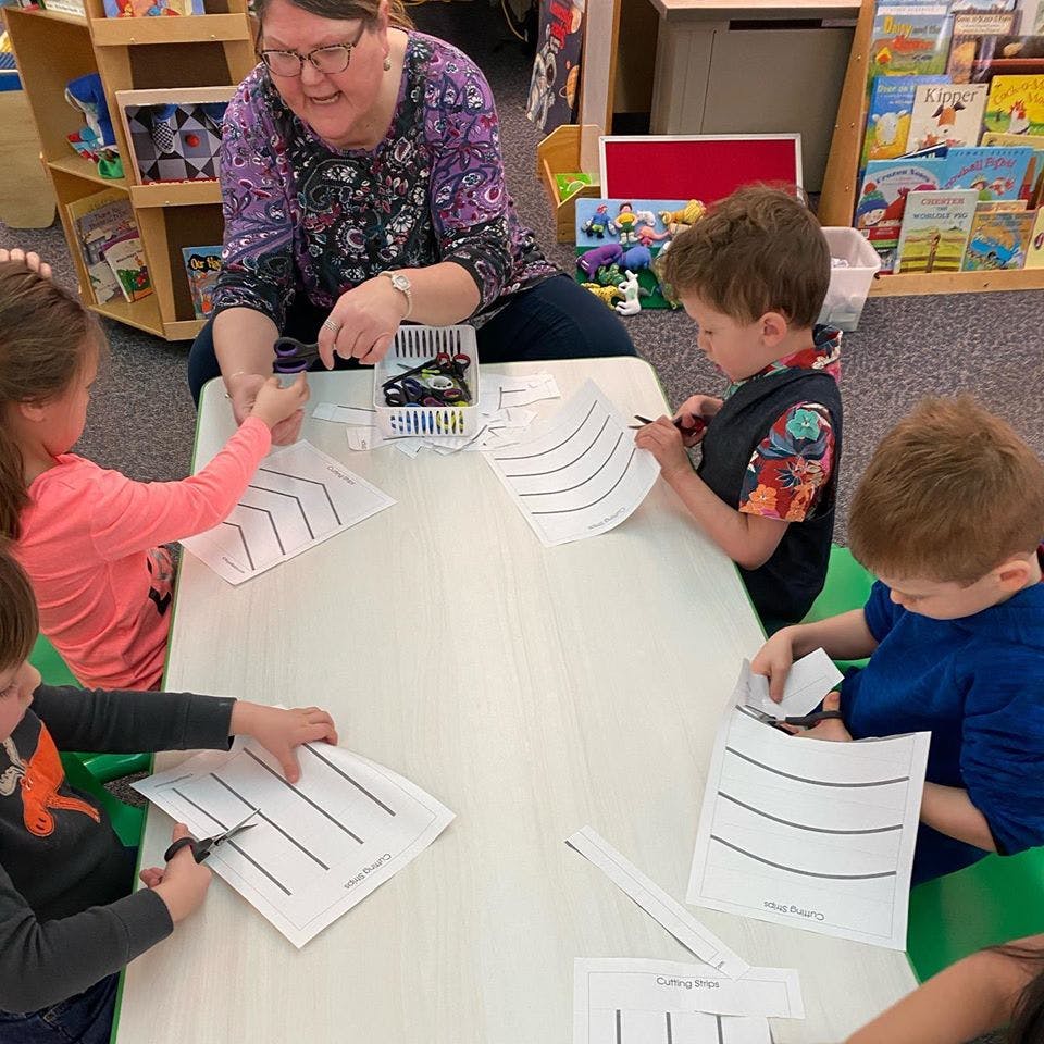 Adult and children cutting paper at a table in a classroom