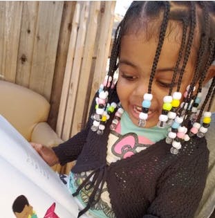 Child with beaded braids looking at a book