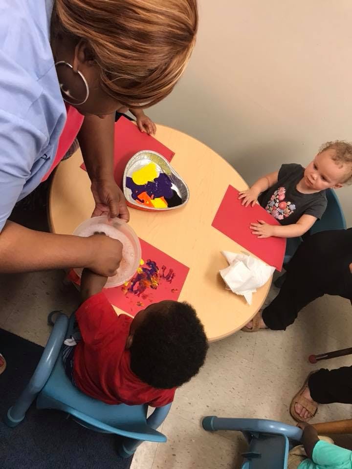 Person helping a child with finger painting at a table