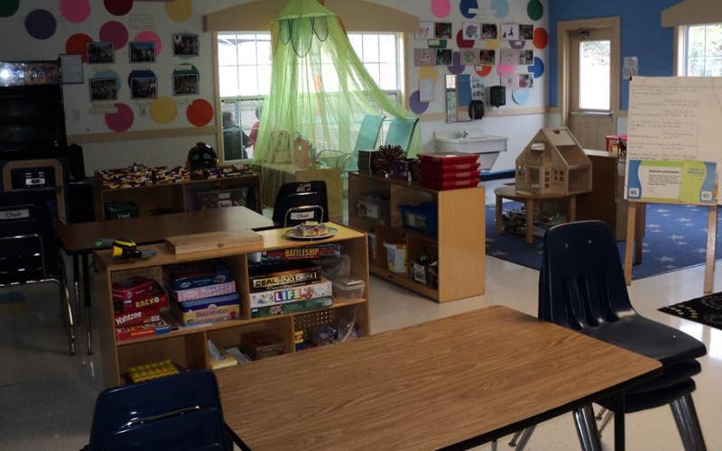 An empty classroom with tables, chairs, bookshelves, and a small sink