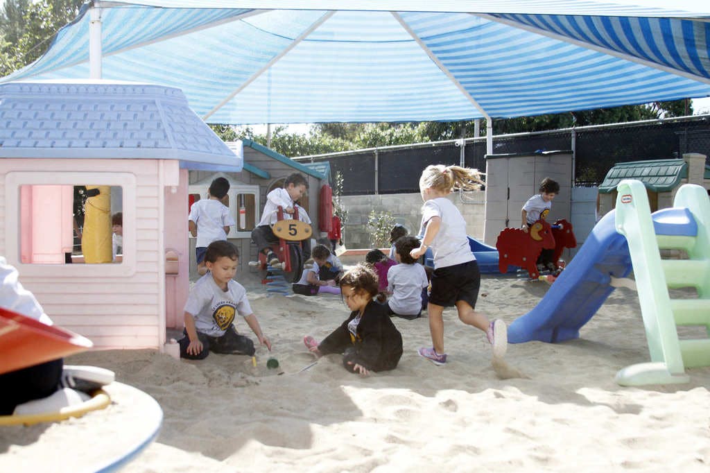 Children playing in a sandbox under a striped canopy