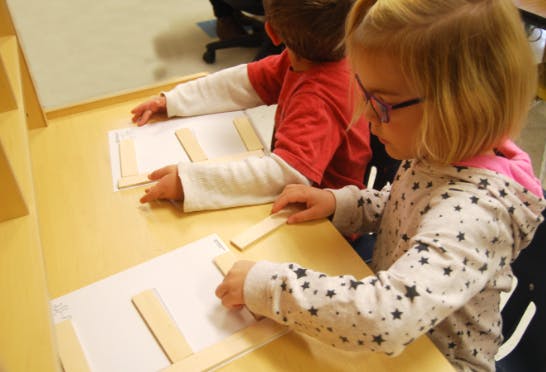Two children working with craft sticks on paper at a table
