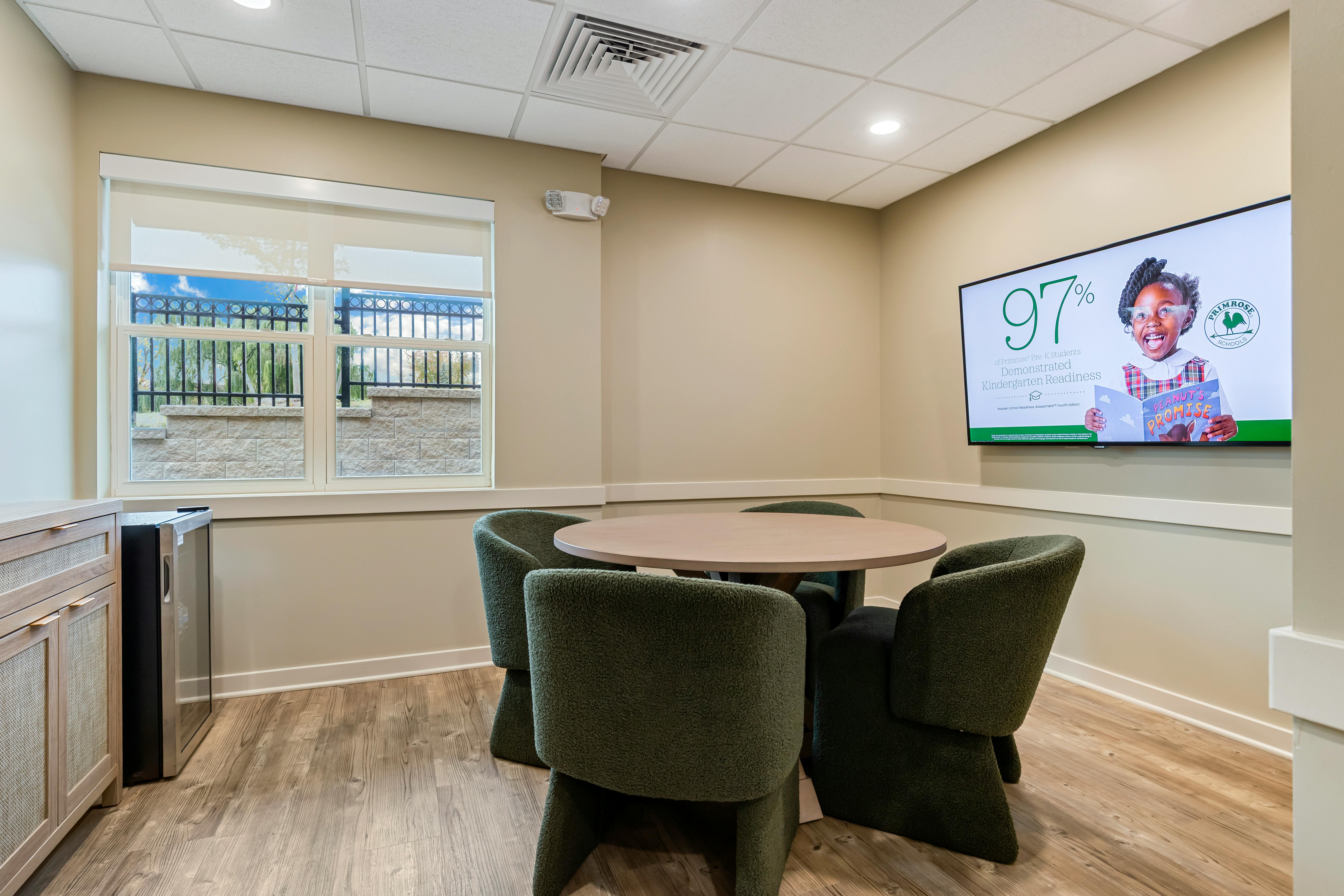 Small meeting room with a round table, four green chairs, and a TV screen