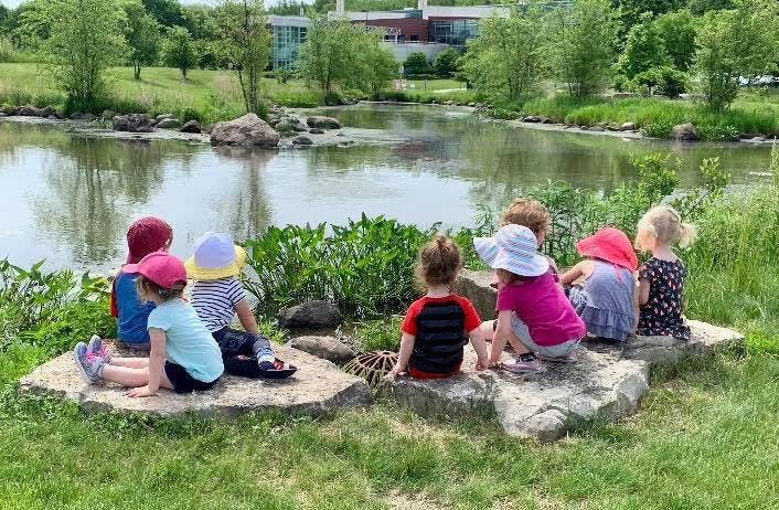 Children sitting on rocks by a pond