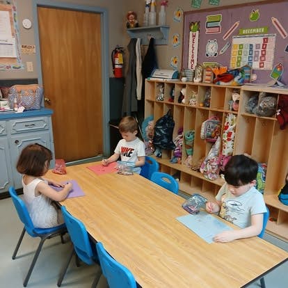 Three children working on paper at a table in a classroom