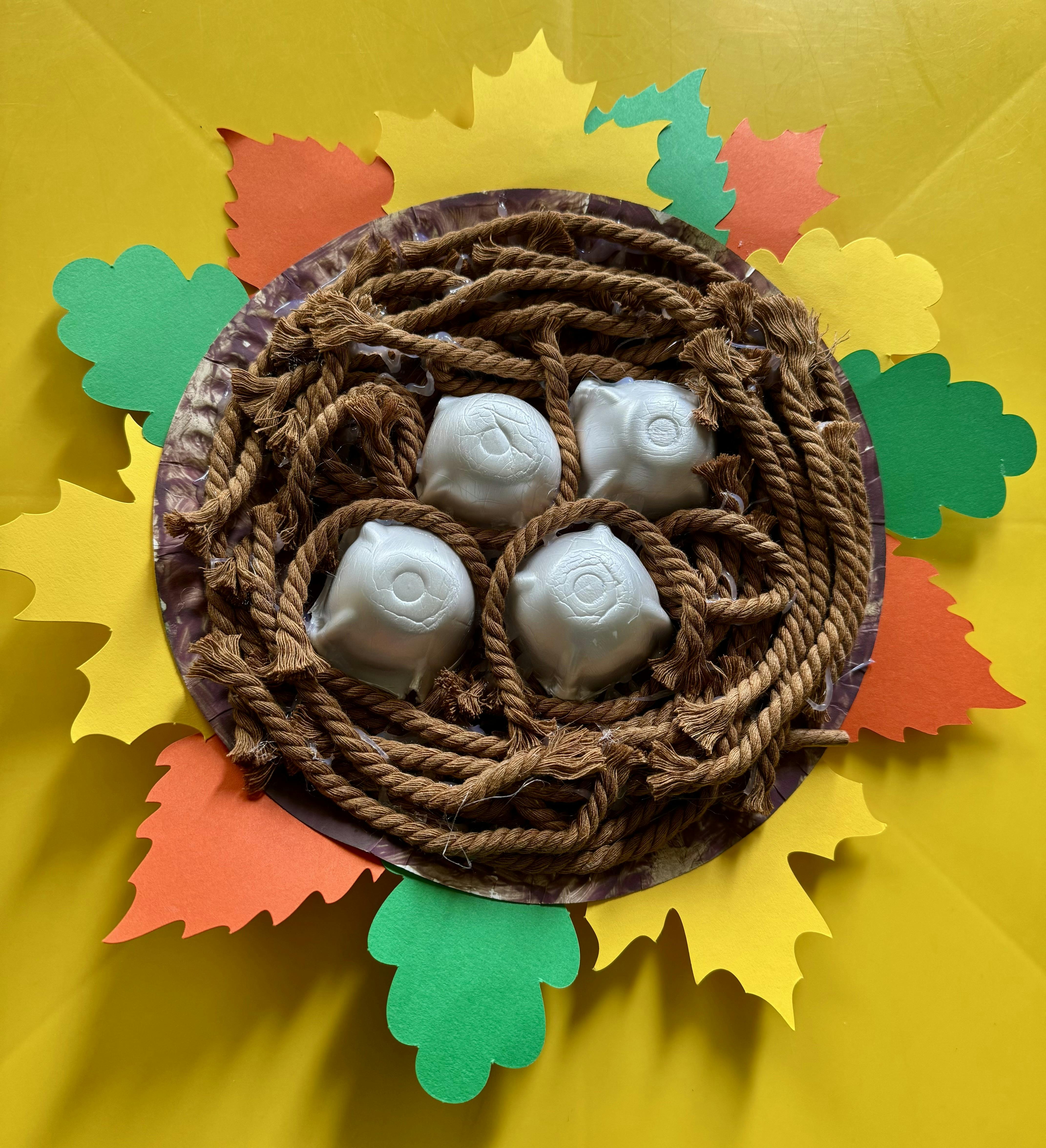 Craft nest with four white egg-like objects and paper leaves