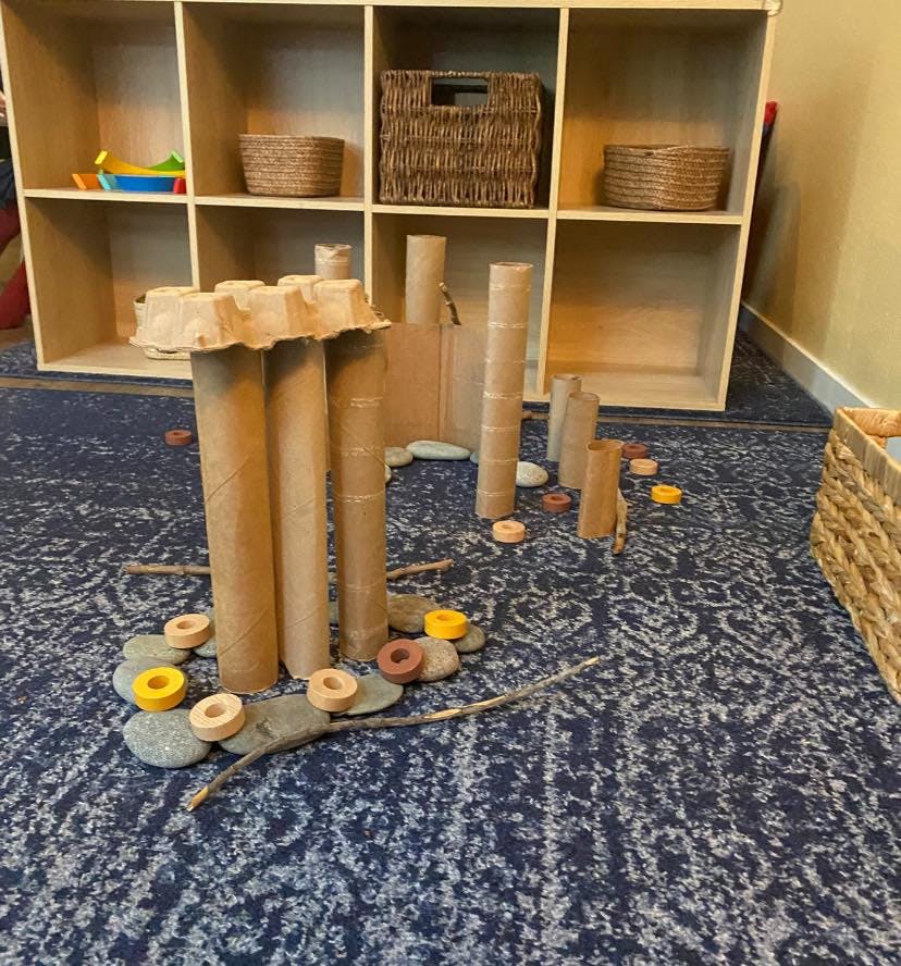 Cardboard tubes and egg carton pieces arranged on a rug with stones and wooden rings