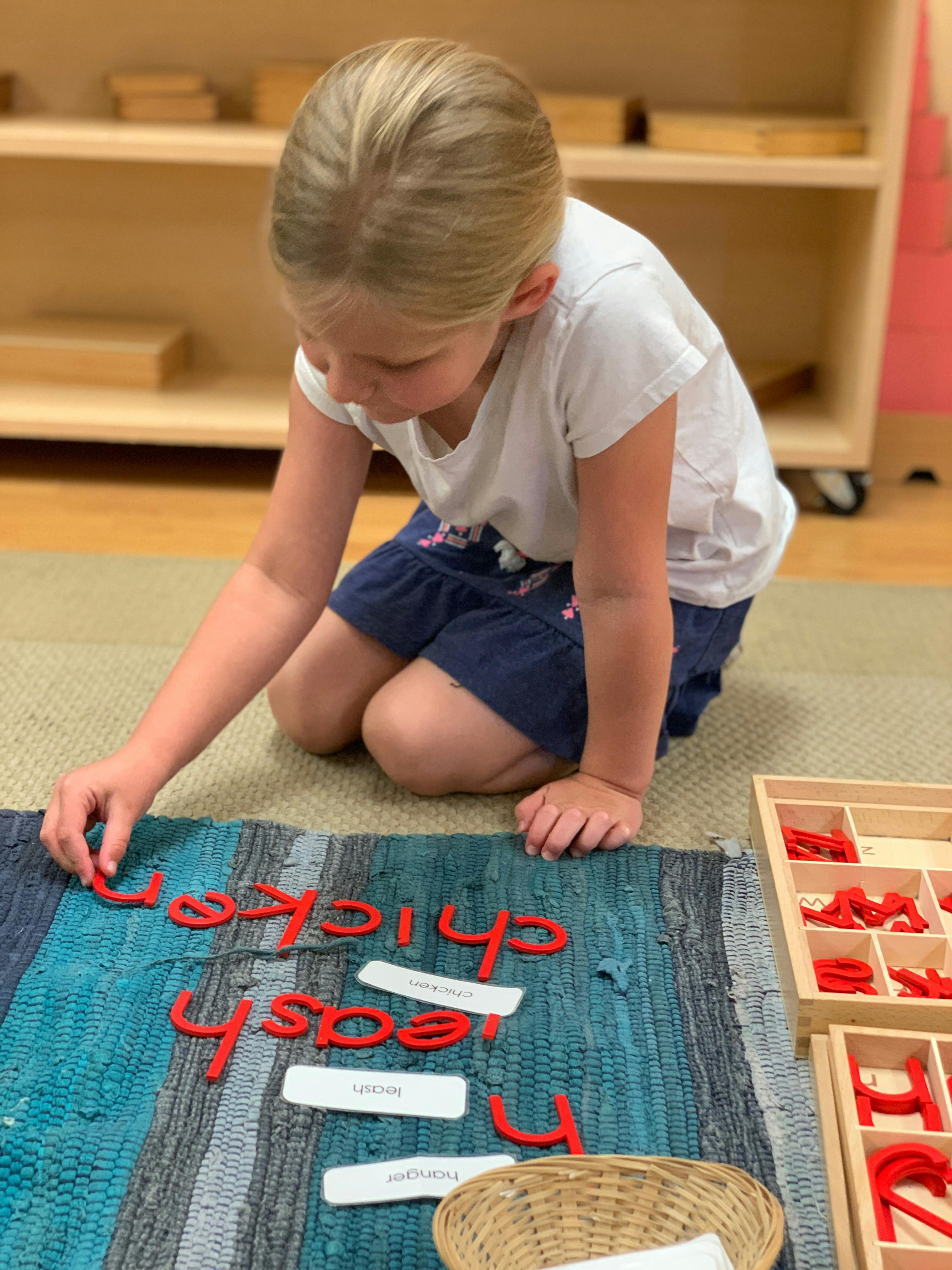 Child kneeling on a rug, arranging red letter cutouts