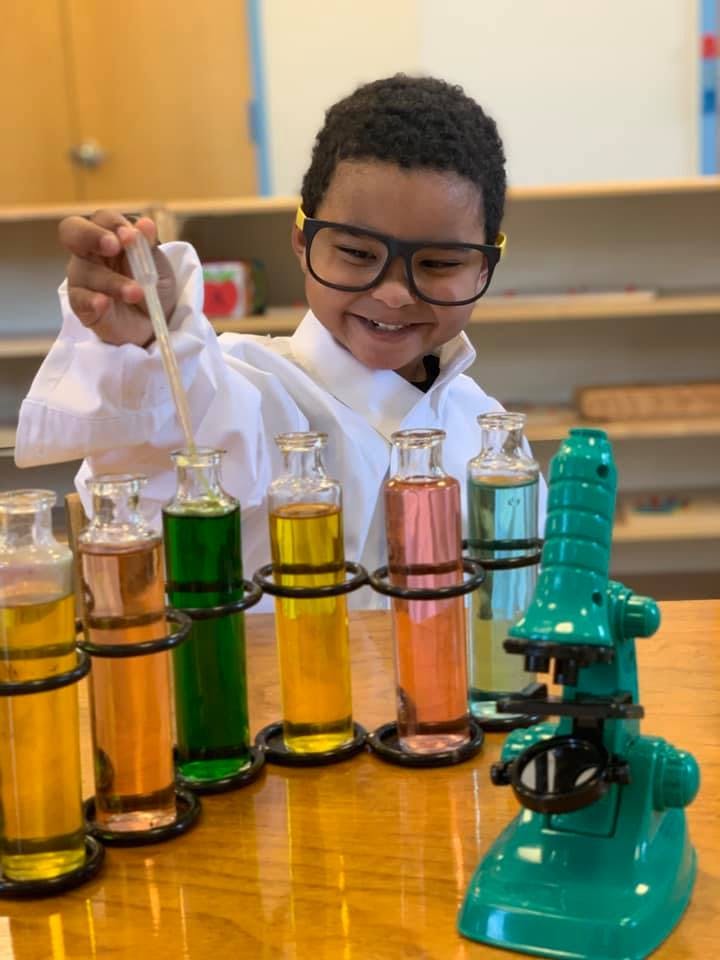 Child in glasses and lab coat using a dropper with colorful liquids