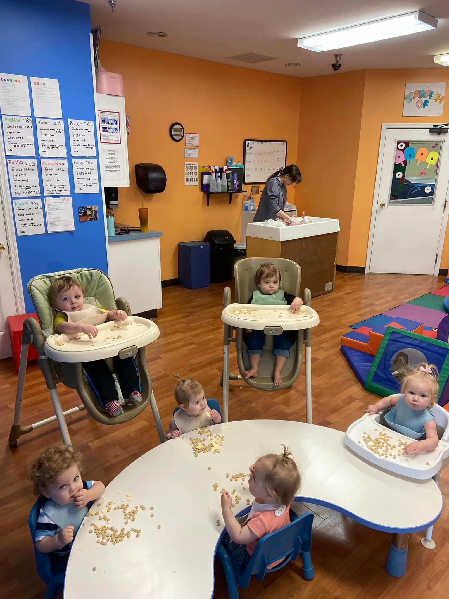 Children in high chairs and at a table with a person in the background
