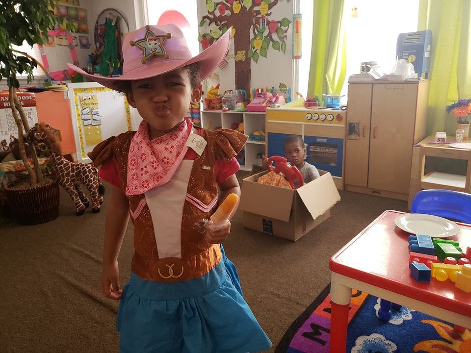 Child in a pink cowboy hat and costume holding a toy in a classroom