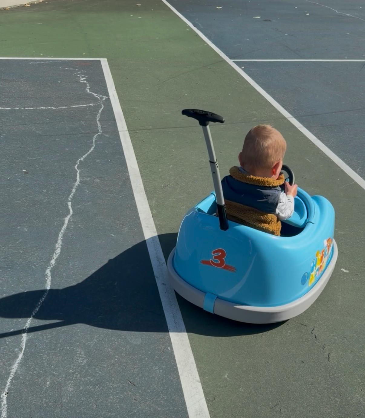 Child sitting in a blue toy car on a sports court
