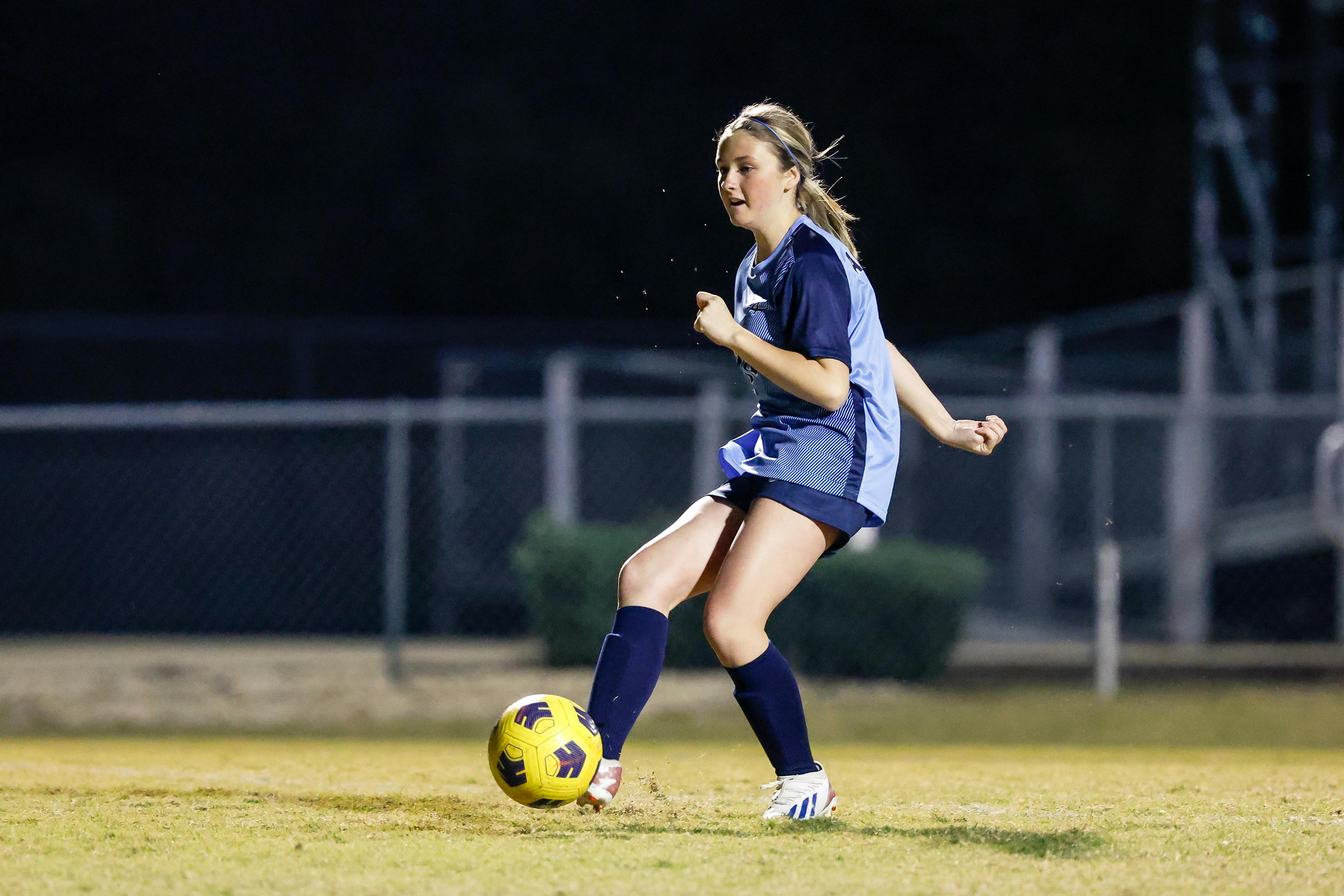 Soccer player in uniform kicking a yellow soccer ball on a field at night