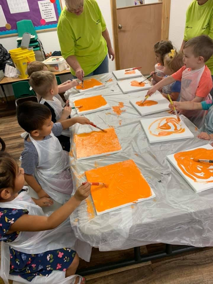 Adult and children painting with orange paint on canvases