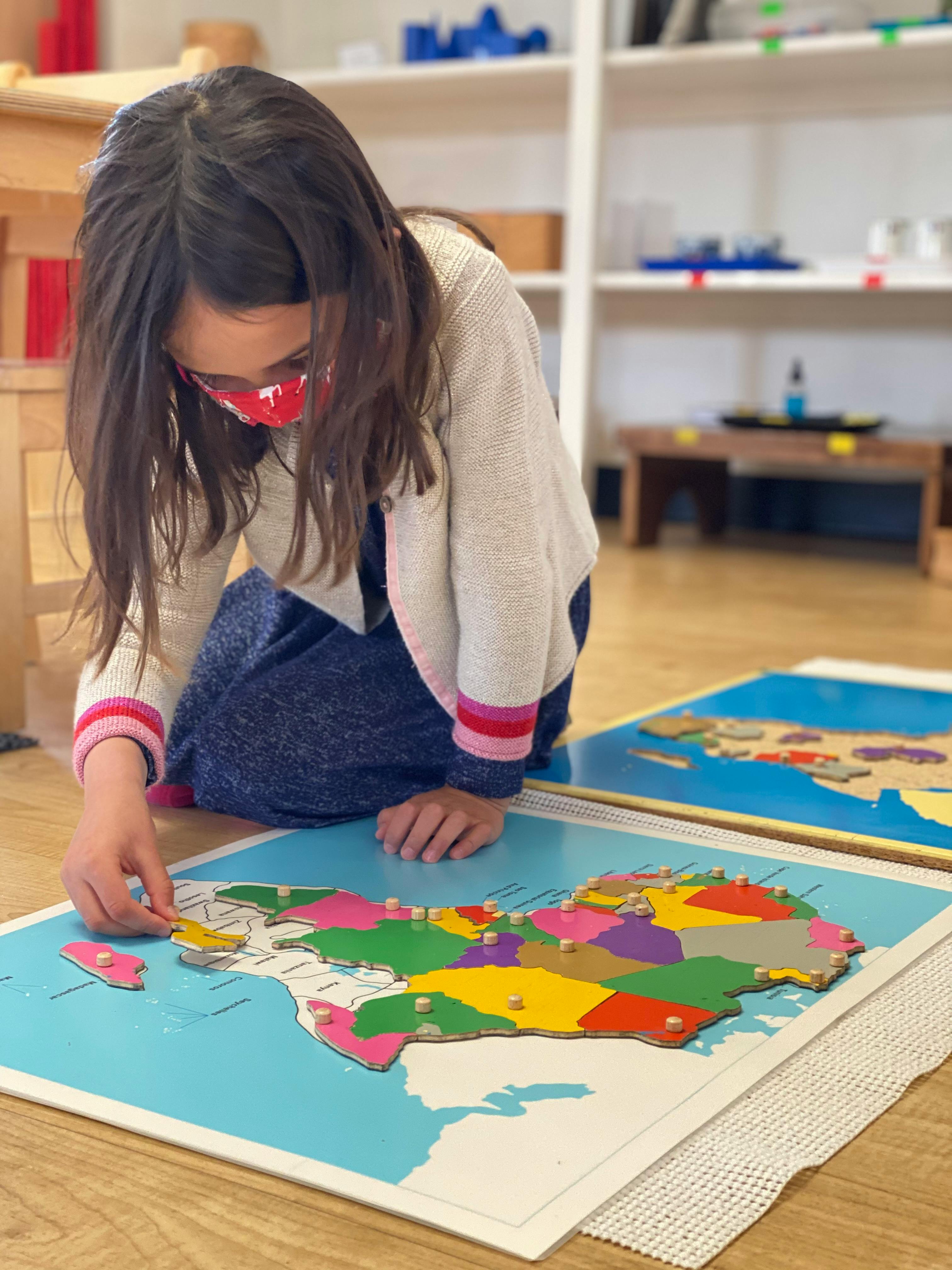 Child in a mask assembling a colorful map puzzle on the floor