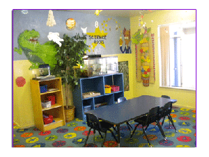 Classroom with a long table and chairs, shelves, and a dinosaur mural