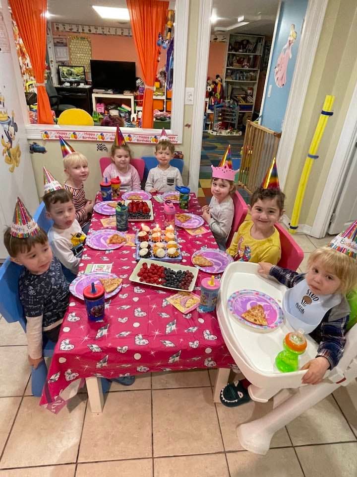 Group of children wearing party hats at a birthday table with pizza and fruit