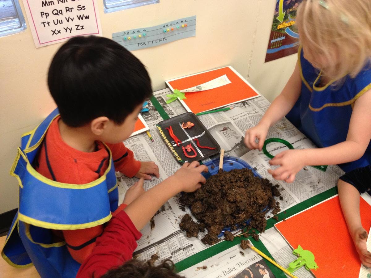 Children playing with dirt on a newspaper-covered table