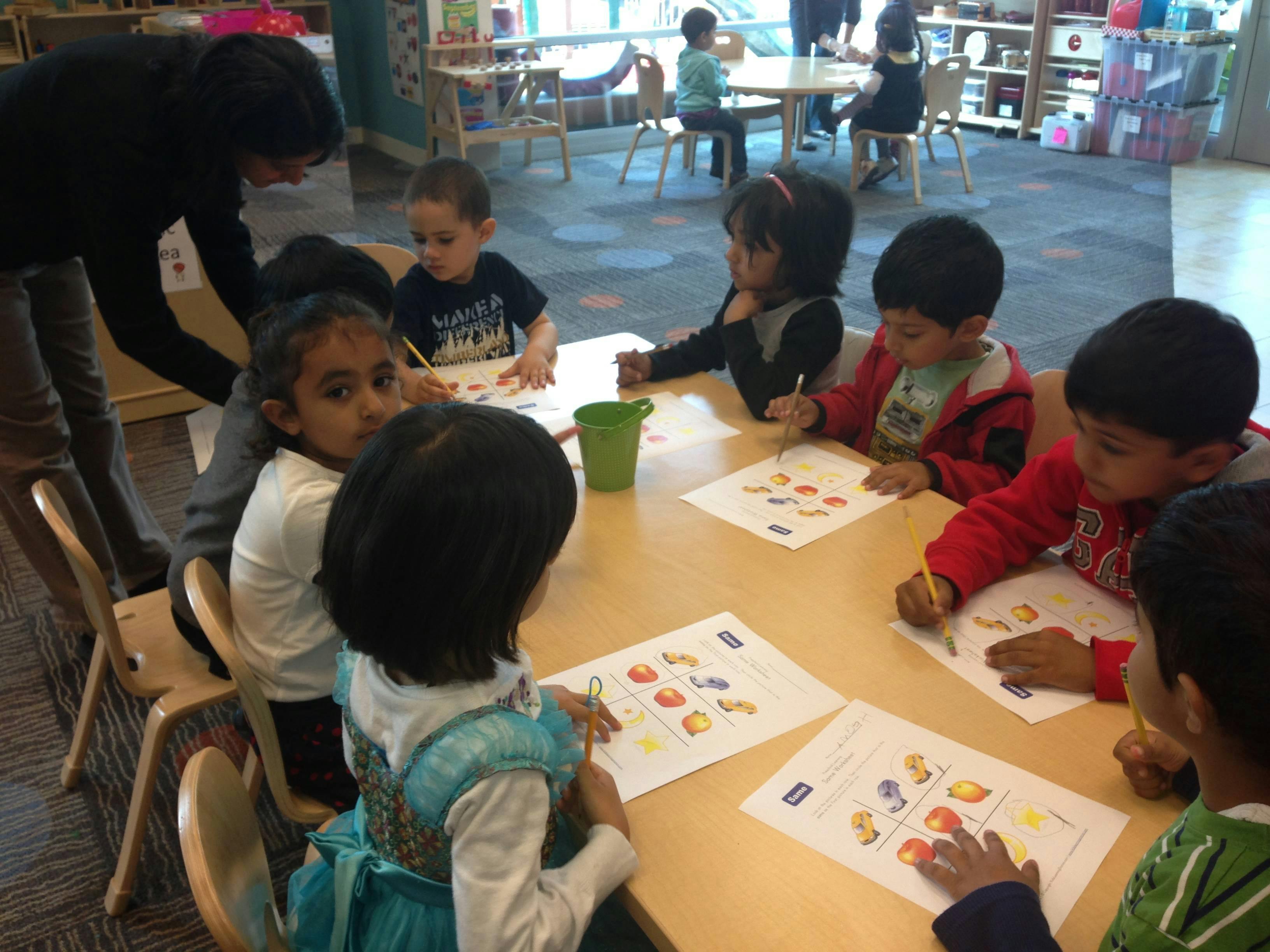 Adult helping children at a table with papers and pencils