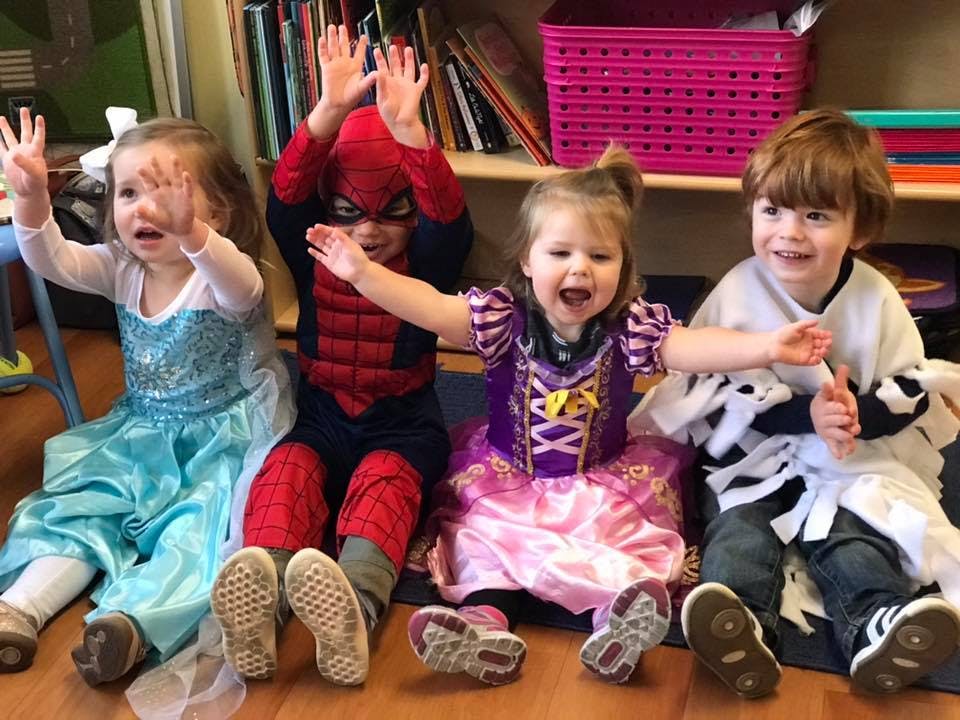 Four children in costumes sitting on the floor with hands raised