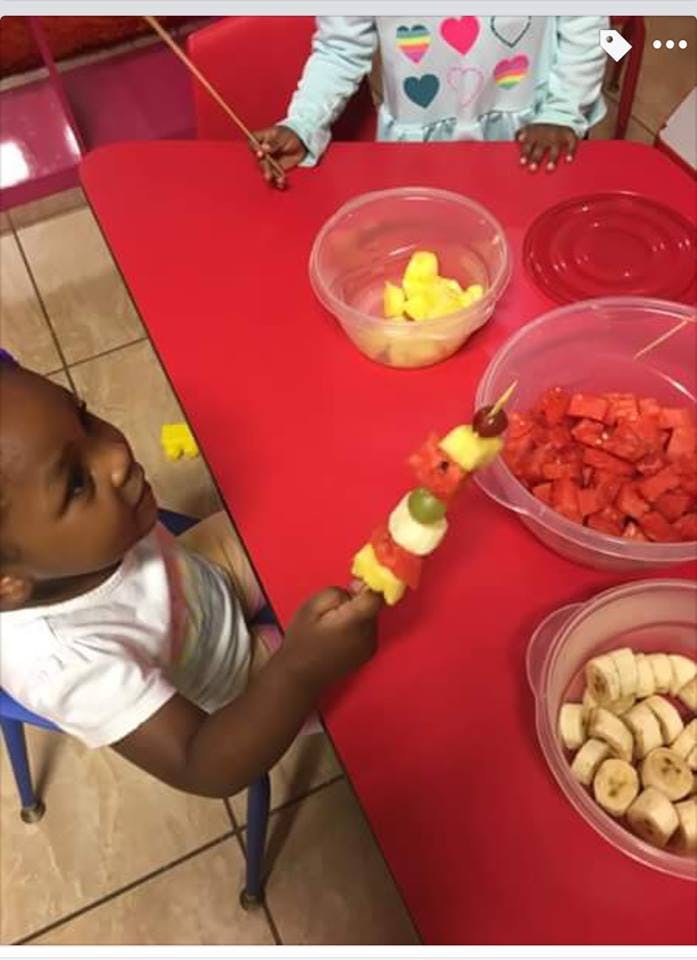 Child holding a fruit skewer at a table with bowls of fruit