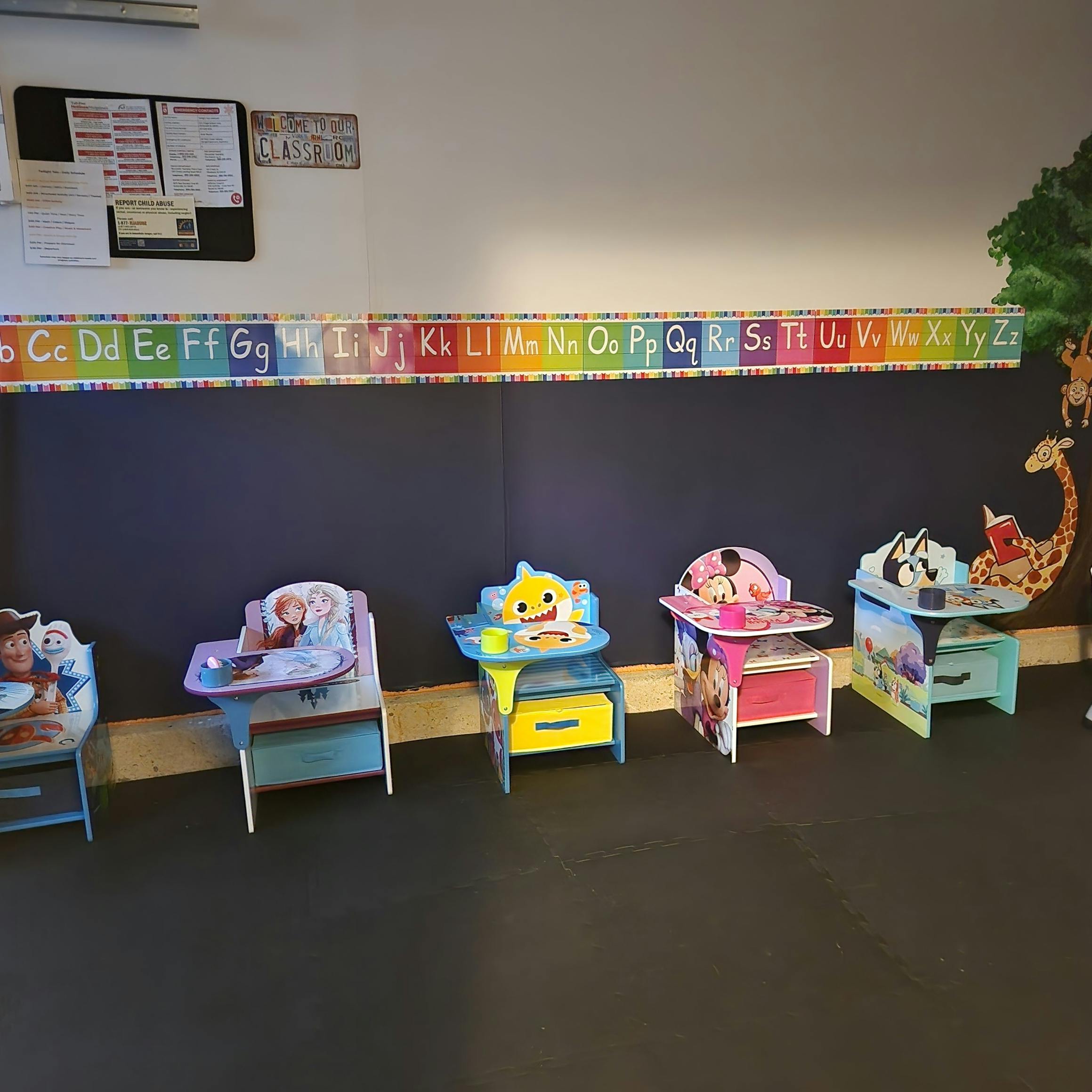 Small colorful desks lined up against a wall with a classroom alphabet border